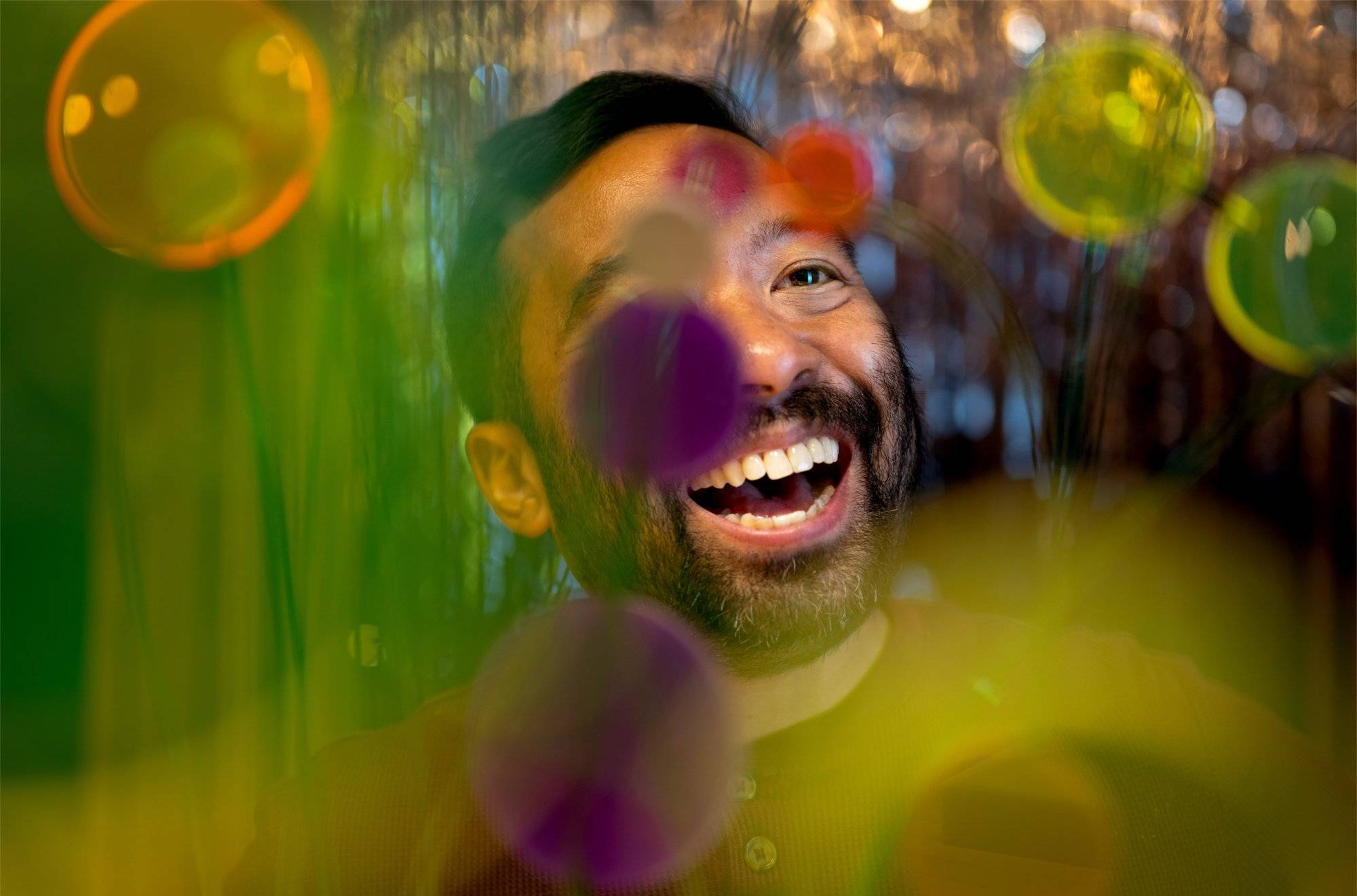 Man standing behind colorful translucent confetti smiles looking off into the distance.